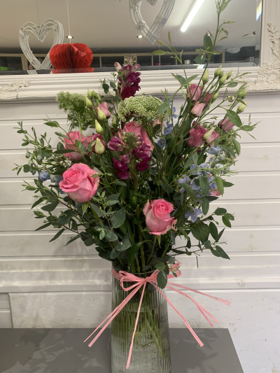 Pink Meadow Mix - A soft, romantic floral arrangement accented with lush greenery. Designed in a clear glass vase and finished with a pink ribbon.